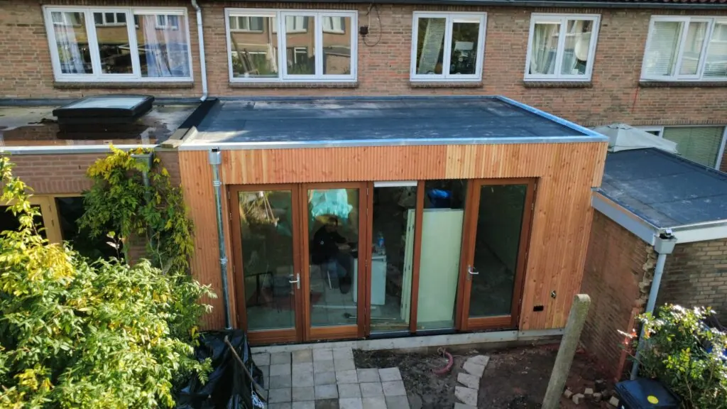 Aanbouw met plat dak, houten gevelbekleding en openslaande deuren